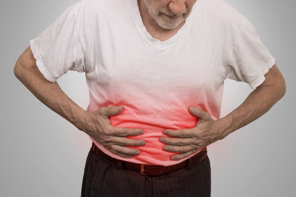 Stomach ache, man placing hands on the abdomen isolated on gray wall background