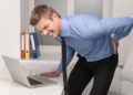 handsome man feeling pain in back. Businessman suffering from back pain at office