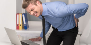 handsome man feeling pain in back. Businessman suffering from back pain at office
