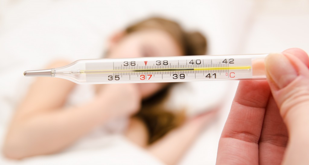 Mother holding thermometer foreground and sick little girl in bed