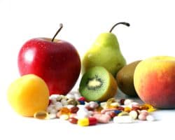 Ein Haufen Vitamintabletten liegt vor verschiedenen Früchten.