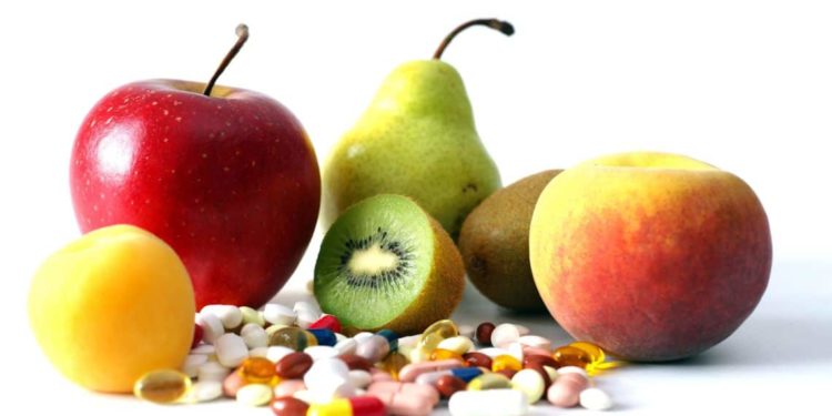 Ein Haufen Vitamintabletten liegt vor verschiedenen Früchten.