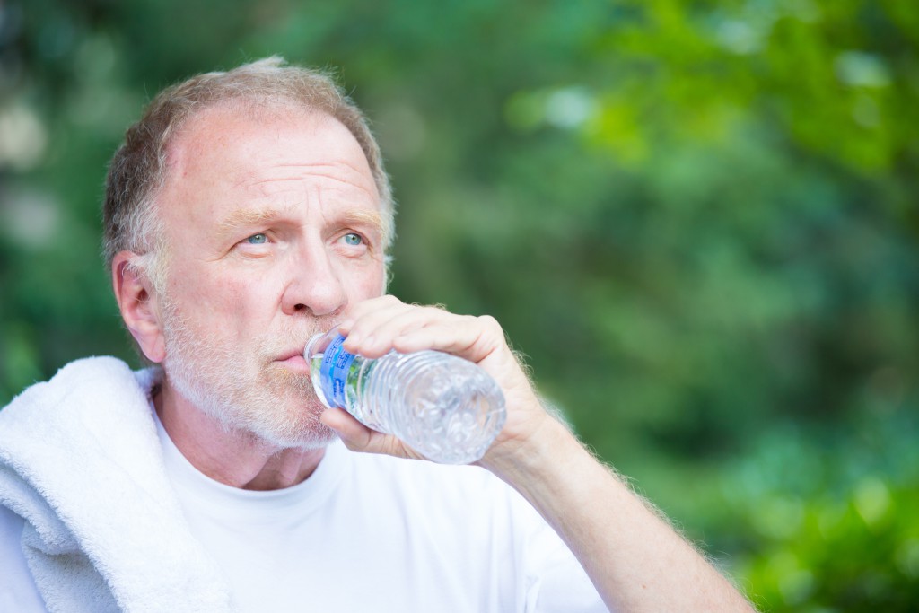 Closeup portrait, thirsty senior mature man drinking water outside, isolated green tree foliage background