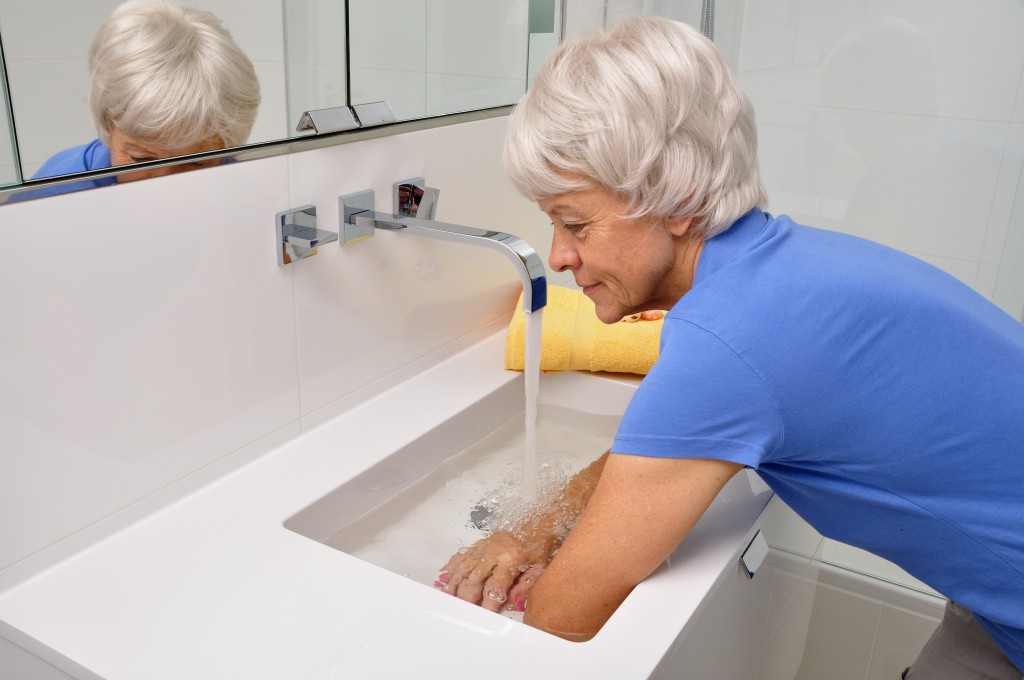 Seniorin macht Wechselbäder im Badezimmerwaschbecken Model released