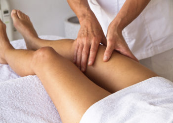 Physiotherapeut behandelt Frau am Oberschenkel.