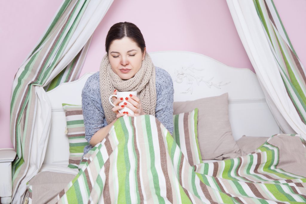 Frau sitz mit einer Tasse krank im Bett 