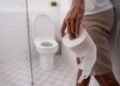 Mann geht mit Kloppapierrolle in Richtung Toilette.