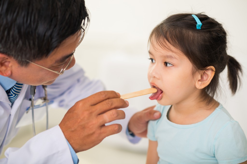 Doctor using tongue depressor to check throat of a girl