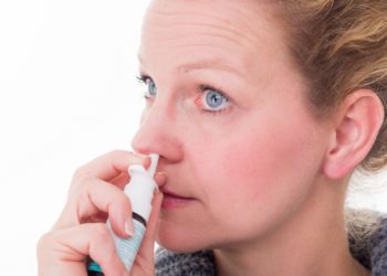 Frau sprüht Nasenspray in ihre Nase