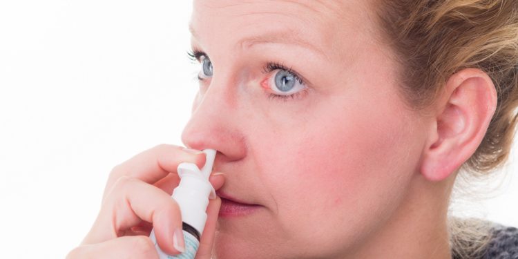 Frau sprüht Nasenspray in ihre Nase