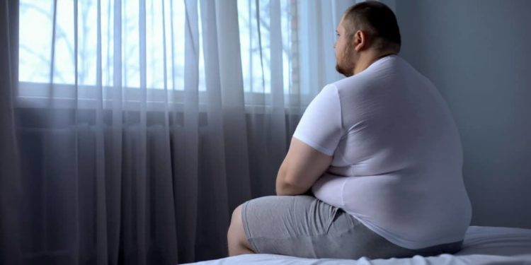 Ein übergewichtiger Mann sitzt auf einem Bett.