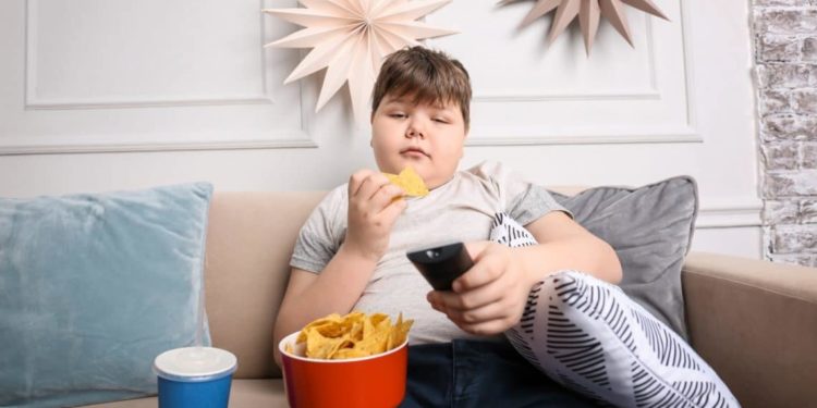 Ein Junge sitzt vorm Fernseher, isst Chips und trinkt Cola.