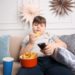 Ein Junge sitzt vorm Fernseher, isst Chips und trinkt Cola.