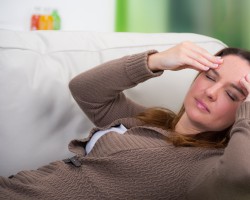 Auf dem Sofa liegende Frau mit Kopfschmerzen massiert ihre Schläfen