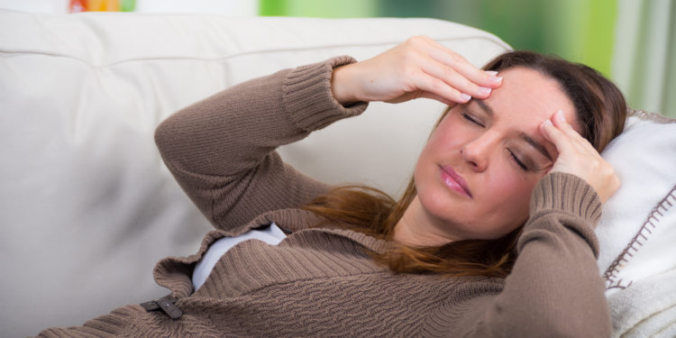 Auf dem Sofa liegende Frau mit Kopfschmerzen massiert ihre Schläfen