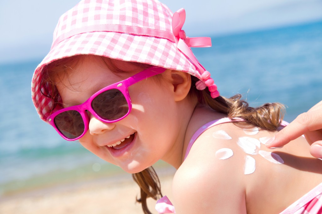 Mom anoints protective cream back a little girl on the beach