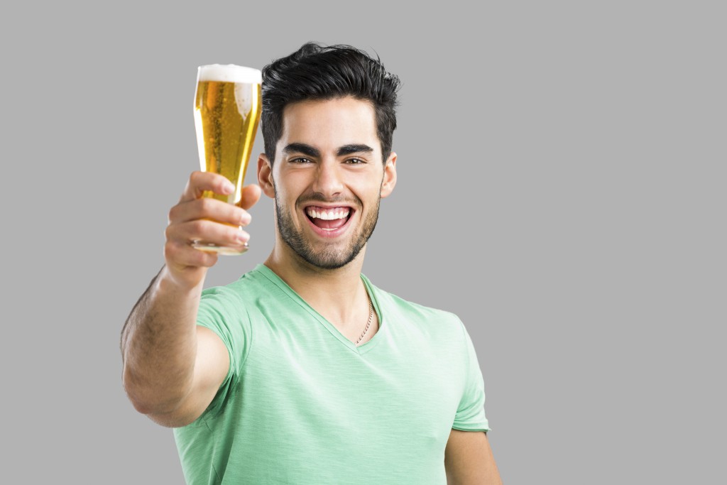 Portrait of handsome young man tasting a draft beer, isolated on gray background