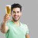 Portrait of handsome young man tasting a draft beer, isolated on gray background