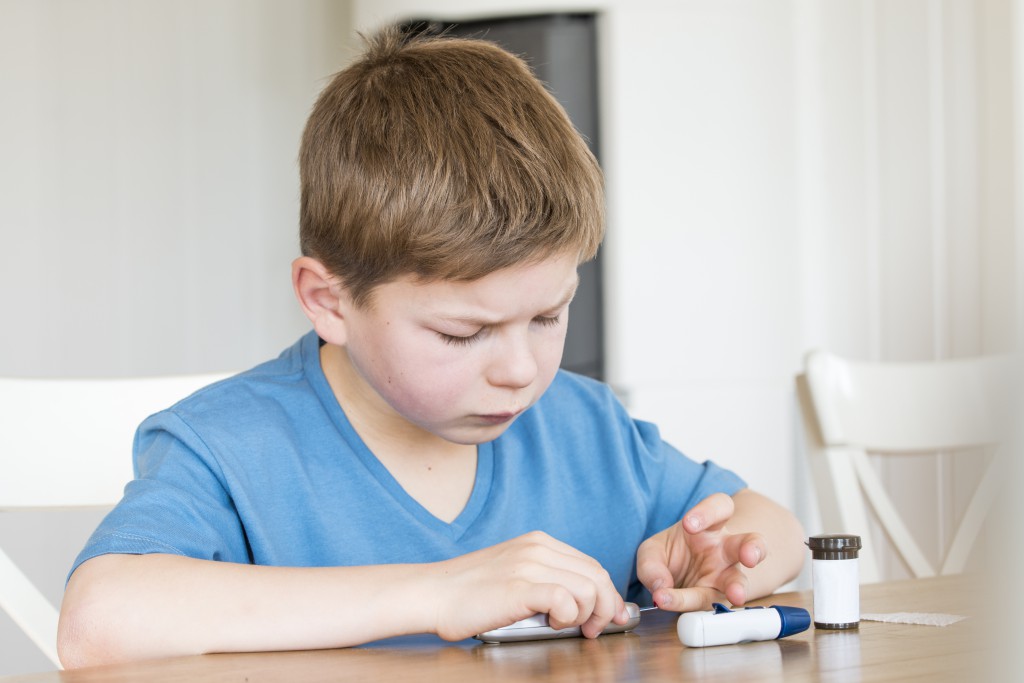 Young boy with diabetes measuring blood sugar.