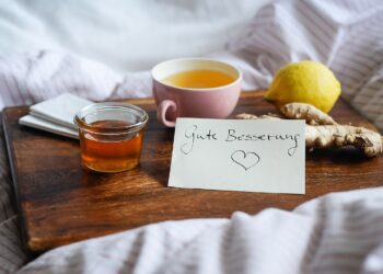 Tee, Zitrone, Ingwer und Honig auf einem Holztablett in einem Bett
