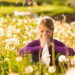 Girl sitting in a meadow with dandelions and has hay fever or allergy