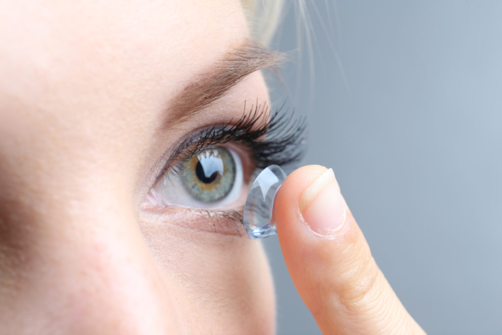 Medicine and vision concept - young woman with contact lens, close up