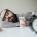 Man with beard in glasses sleeps in office on the table over laptop with coffee in hand