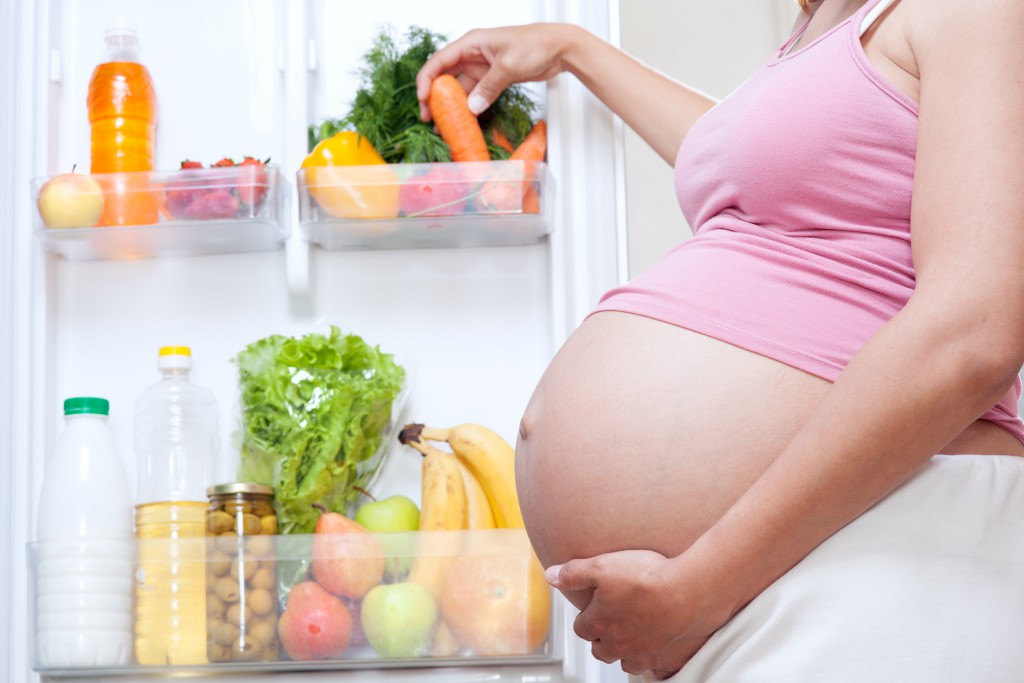 pregnant woman and refrigerator with health food vegetables and fruits