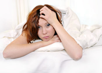 Frau liegt mit Kopfschmerzen im Bett