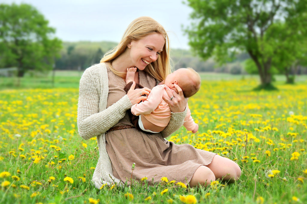 Junge Frau kitzelt ihr Baby auf einer Blumenwiese