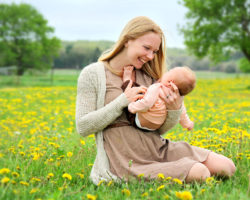 Junge Frau kitzelt ihr Baby auf einer Blumenwiese