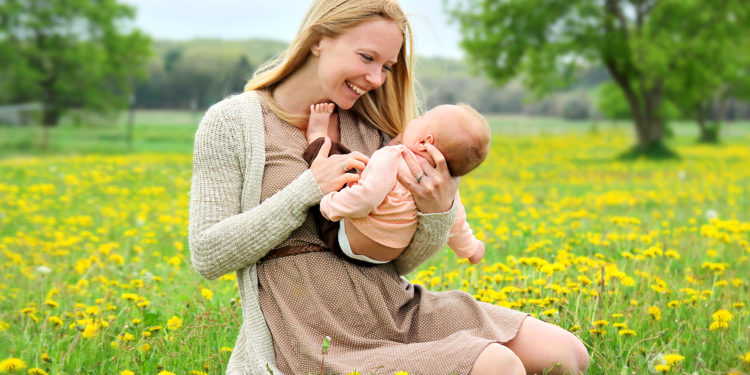 Junge Frau kitzelt ihr Baby auf einer Blumenwiese