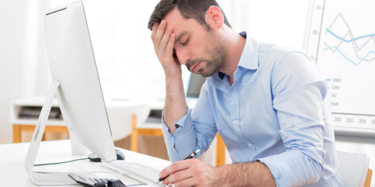 Ein Mann sitzt erschöpft im Büro und hält sich die Hand an die Stirn.