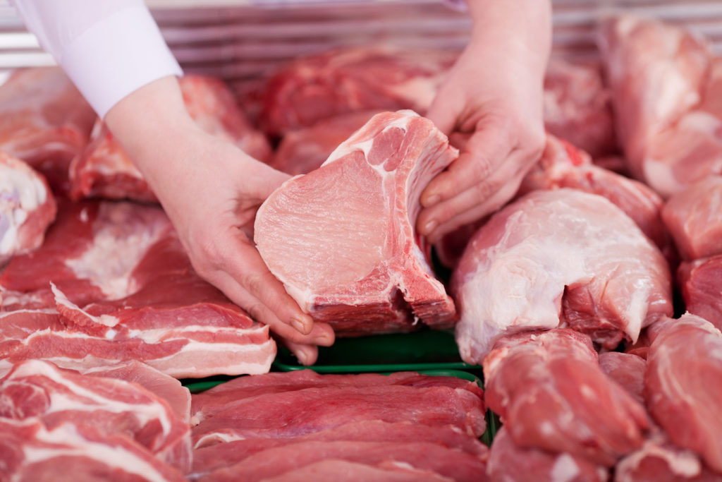 Eine Person zeigt ein Stück rohes Fleisch aus einer mit rohem Fleisch gefüllten Theke