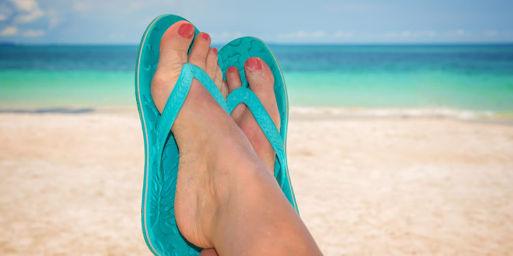 Frauenfüße in Flip-Flops am Meeresstrand