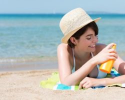 Junge Frau am Strand trägt Sonnenschutzmittel auf die Haut auf