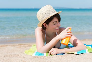 Junge Frau am Strand trägt Sonnenschutzmittel auf die Haut auf