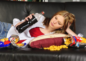 Frau mit Cola und Snacks auf dem Sofa.