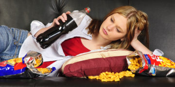 Frau mit Cola und Snacks auf dem Sofa.