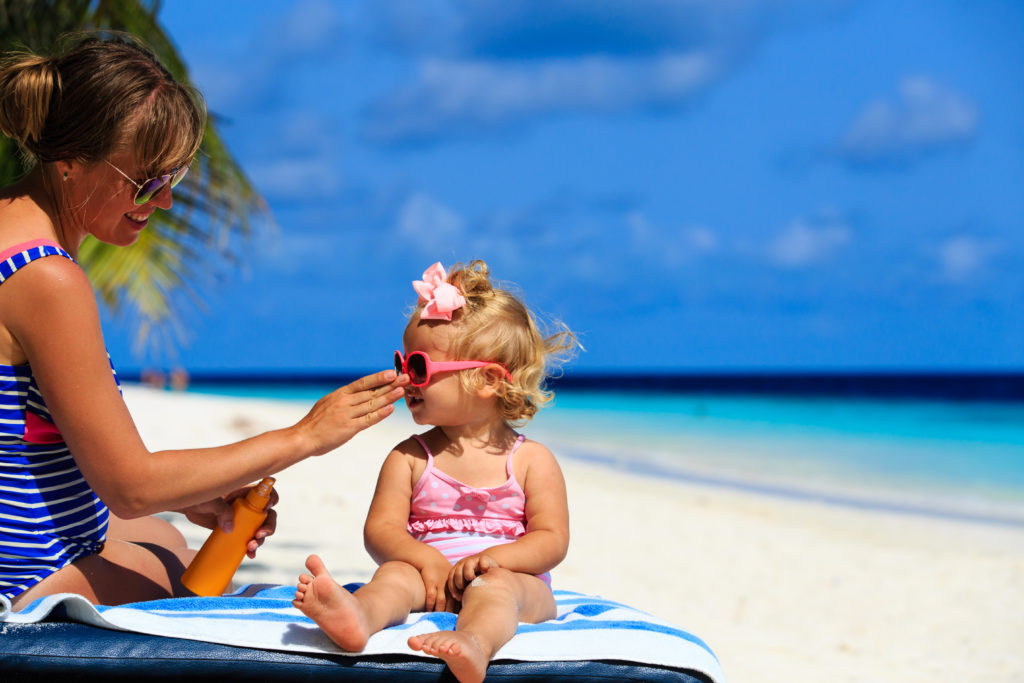 Mutter cremt ihre Tochter am Strand mit Sonnenschutzmittel ein