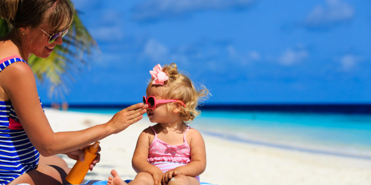Mutter cremt ihre Tochter am Strand mit Sonnenschutzmittel ein