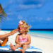 Mutter cremt ihre Tochter am Strand mit Sonnenschutzmittel ein