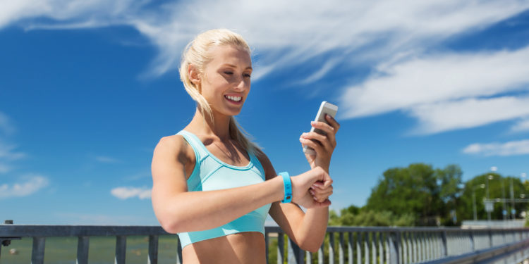 Frau mit Fitnessarmband schaut auf ihr Smartphone.