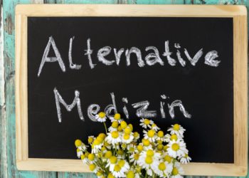 Ein Strauß Margeriten vor einer Tafel mit der Aufschrift: Alternative Medizin