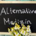 Ein Strauß Margeriten vor einer Tafel mit der Aufschrift: Alternative Medizin