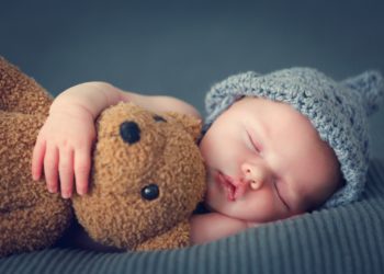 Baby schläft mit Teddybär im Arm
