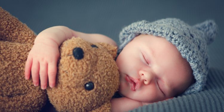 Baby schläft mit Teddybär im Arm