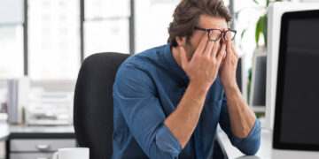 Mann im Büro reibt sich die müden Augen.