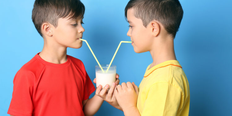 Zwillingsbrüder trinken mit Strohhalmen Milch aus einem gemeinsamen Glas