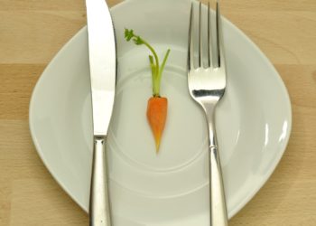 Eine kleine Möhre mit Messer und Gabel auf einem Teller
